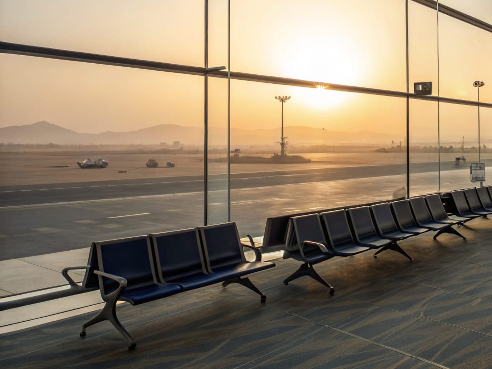 An empty airport gate lounge at dawn with the sun low over a desert horizon