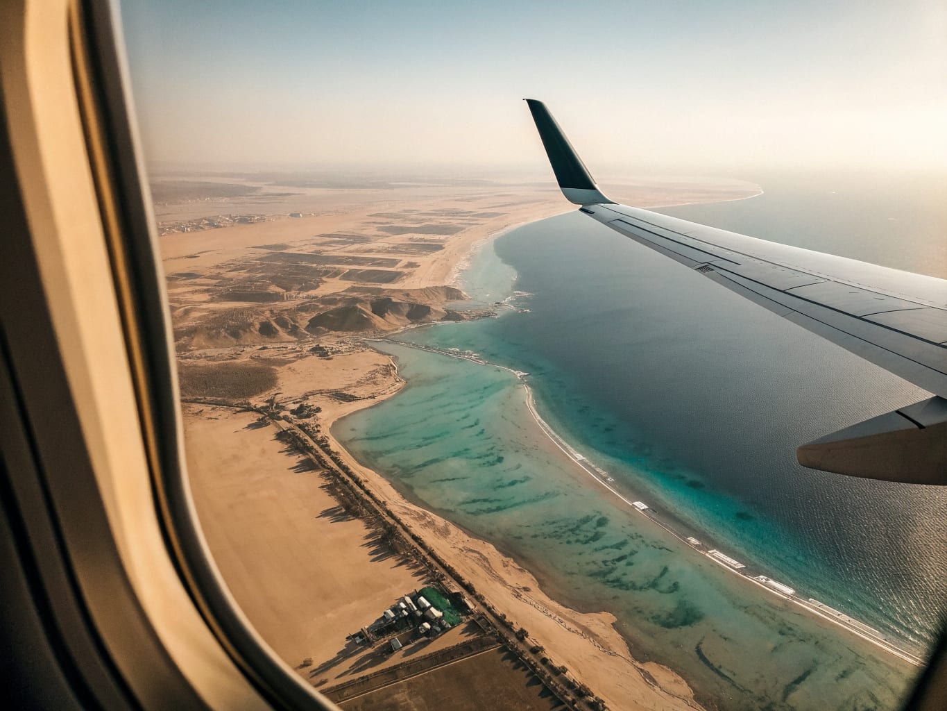 View from an aircraft window over a desert coastline and pale shallows