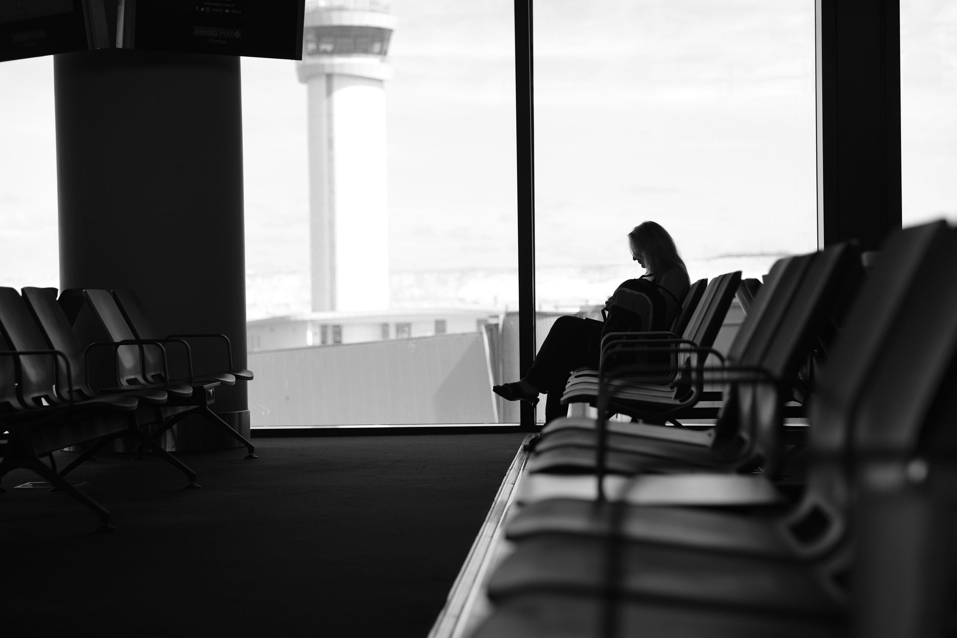 A traveller silhouetted against an airport window beside rows of seats