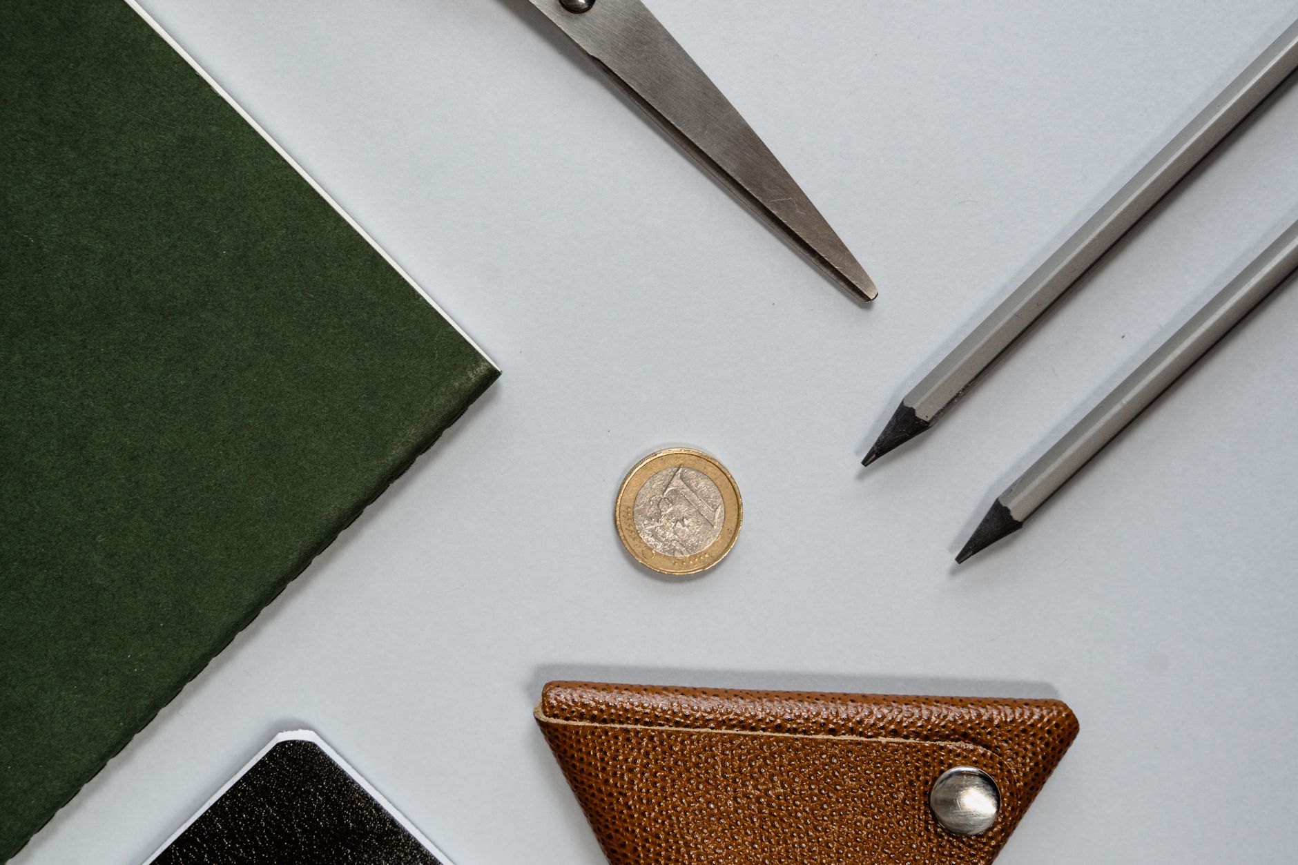 A leather coin pouch, a coin and pencils on a plain desk