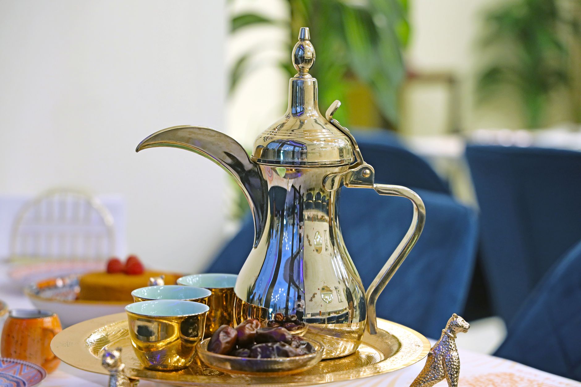 A polished dallah (Arabic coffee pot) on a gold tray with small cups and a dish of dates.
