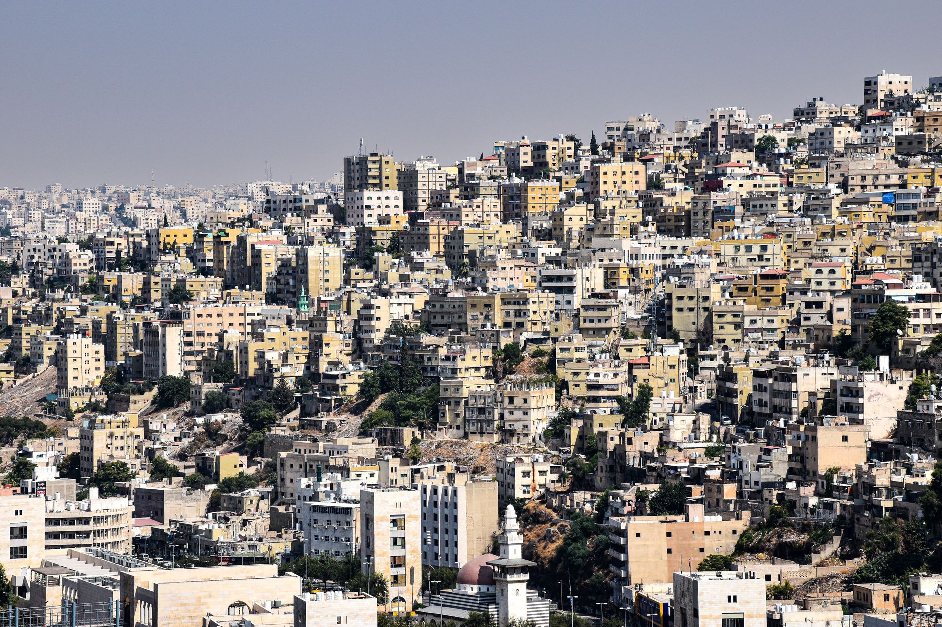 Pale stone houses stacked across the hills of Amman under a clear sky