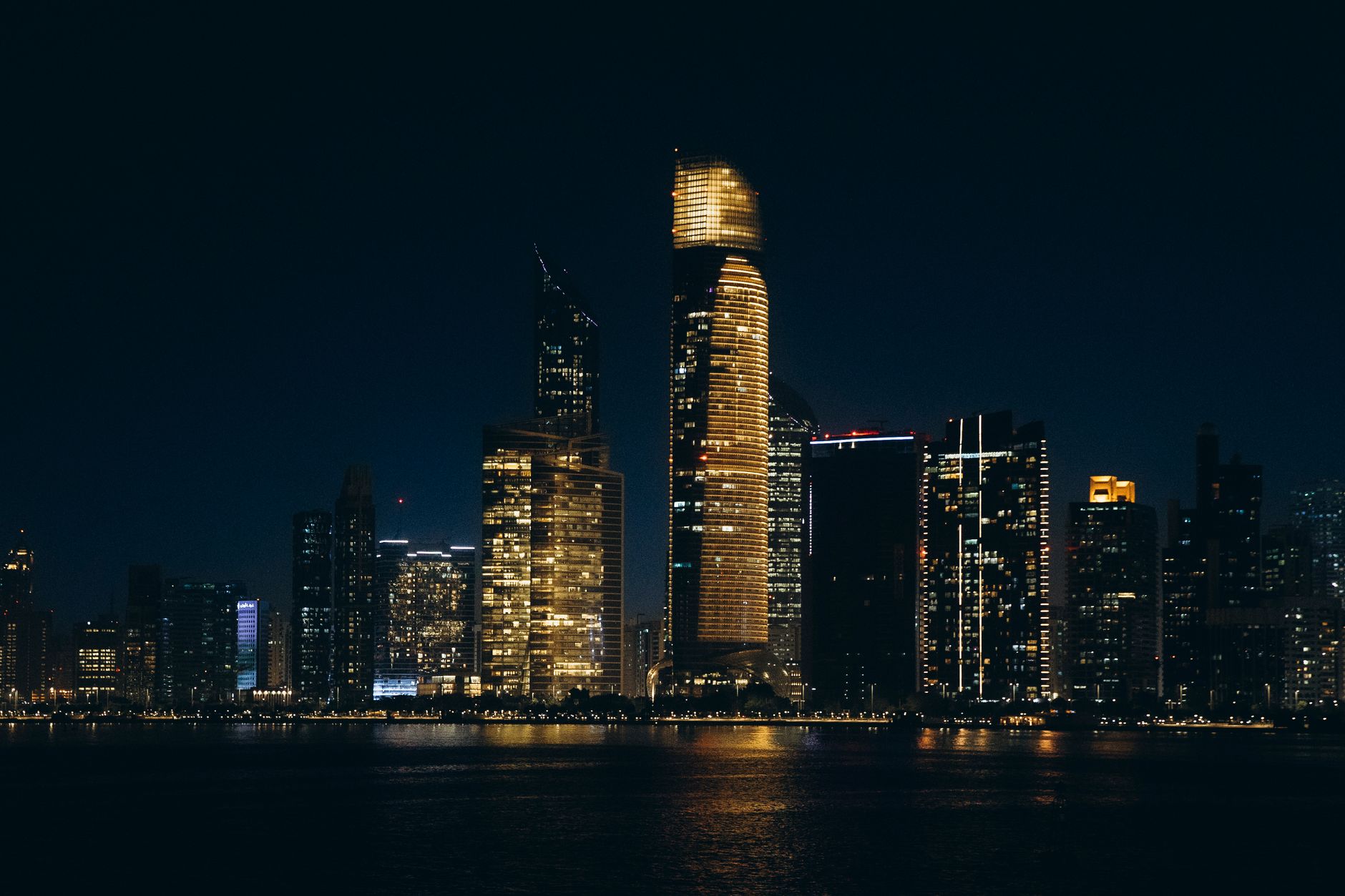 The Abu Dhabi skyline lit up at night, seen across the water from the Corniche