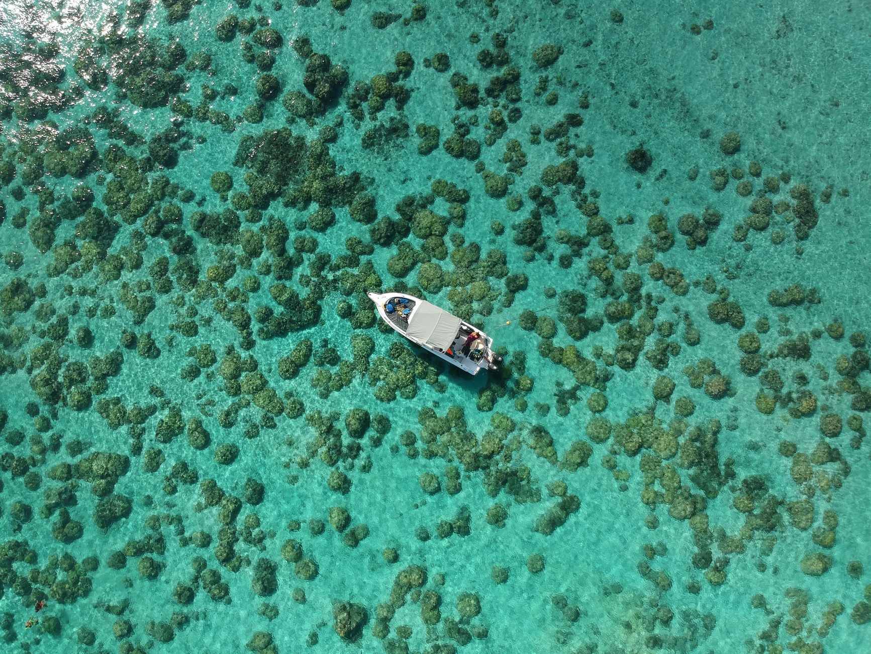 A small boat over clear turquoise shallows, seen from above