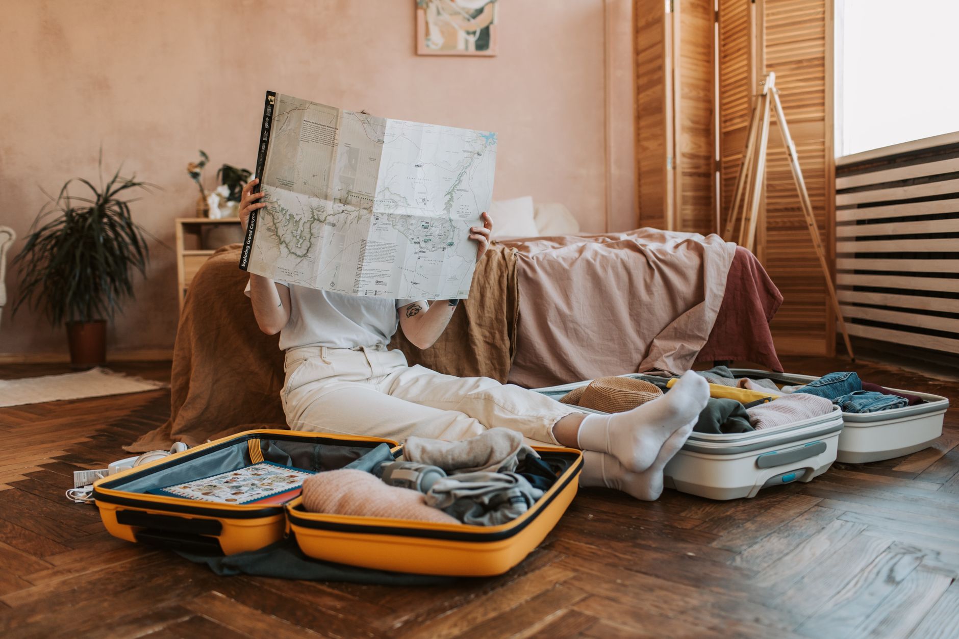 Open suitcases being packed on a bedroom floor while someone reads a travel map, illustrating a credit-card welcome offer paid as a travel voucher.