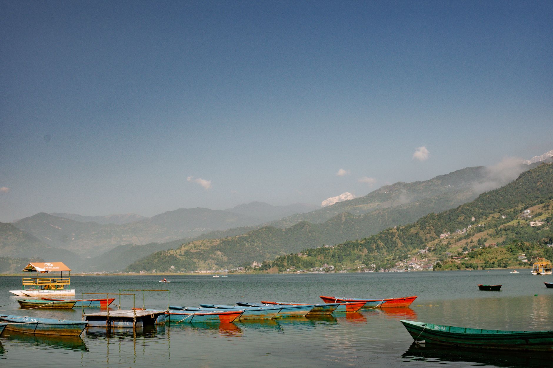 Rowing boats moored on Phewa Lake at Pokhara, Nepal, below forested hills.