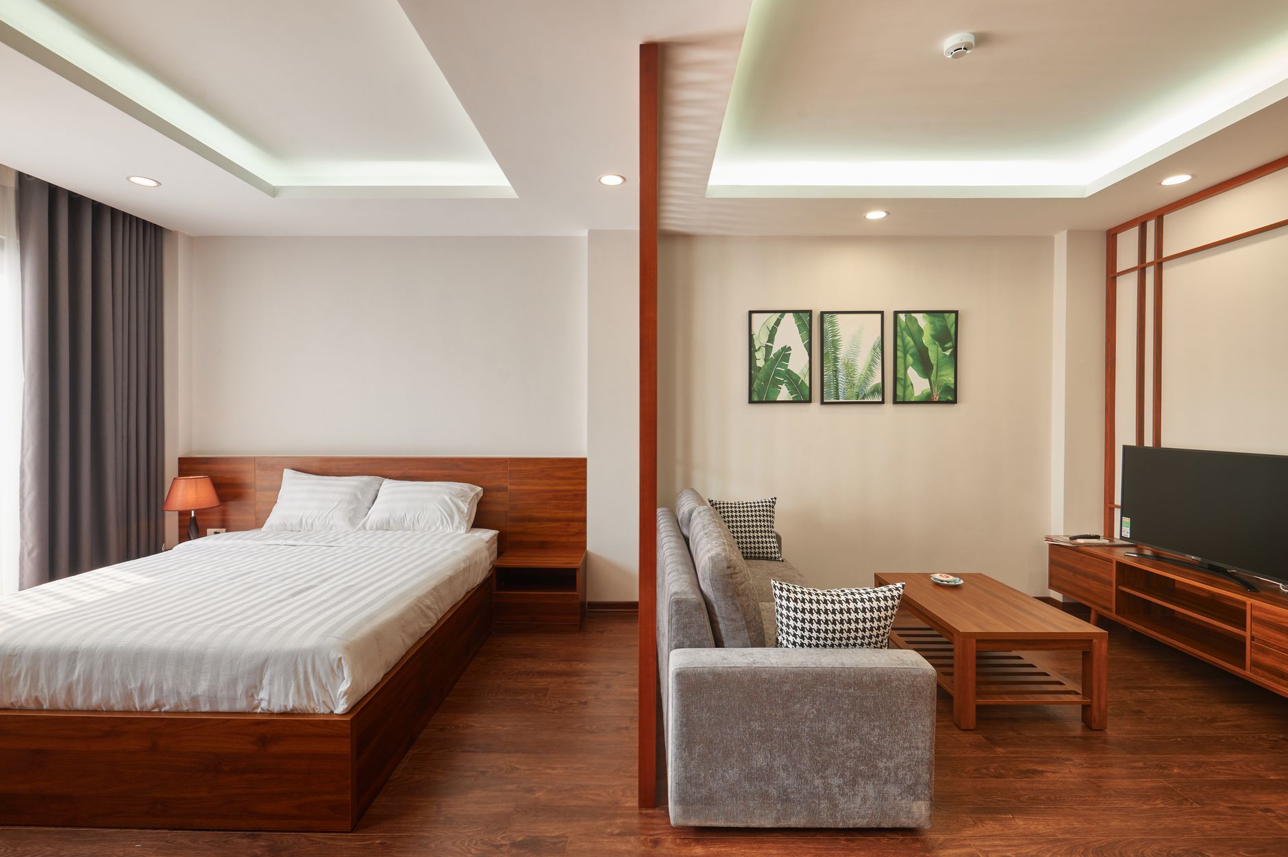 A hotel room with a double bed, a grey sofa and a wooden coffee table in soft light
