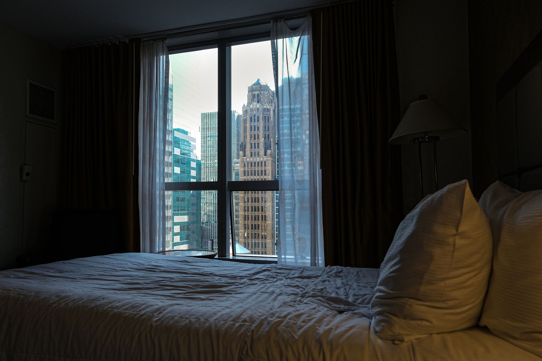 A hotel room with a large window looking out on city skyscrapers.