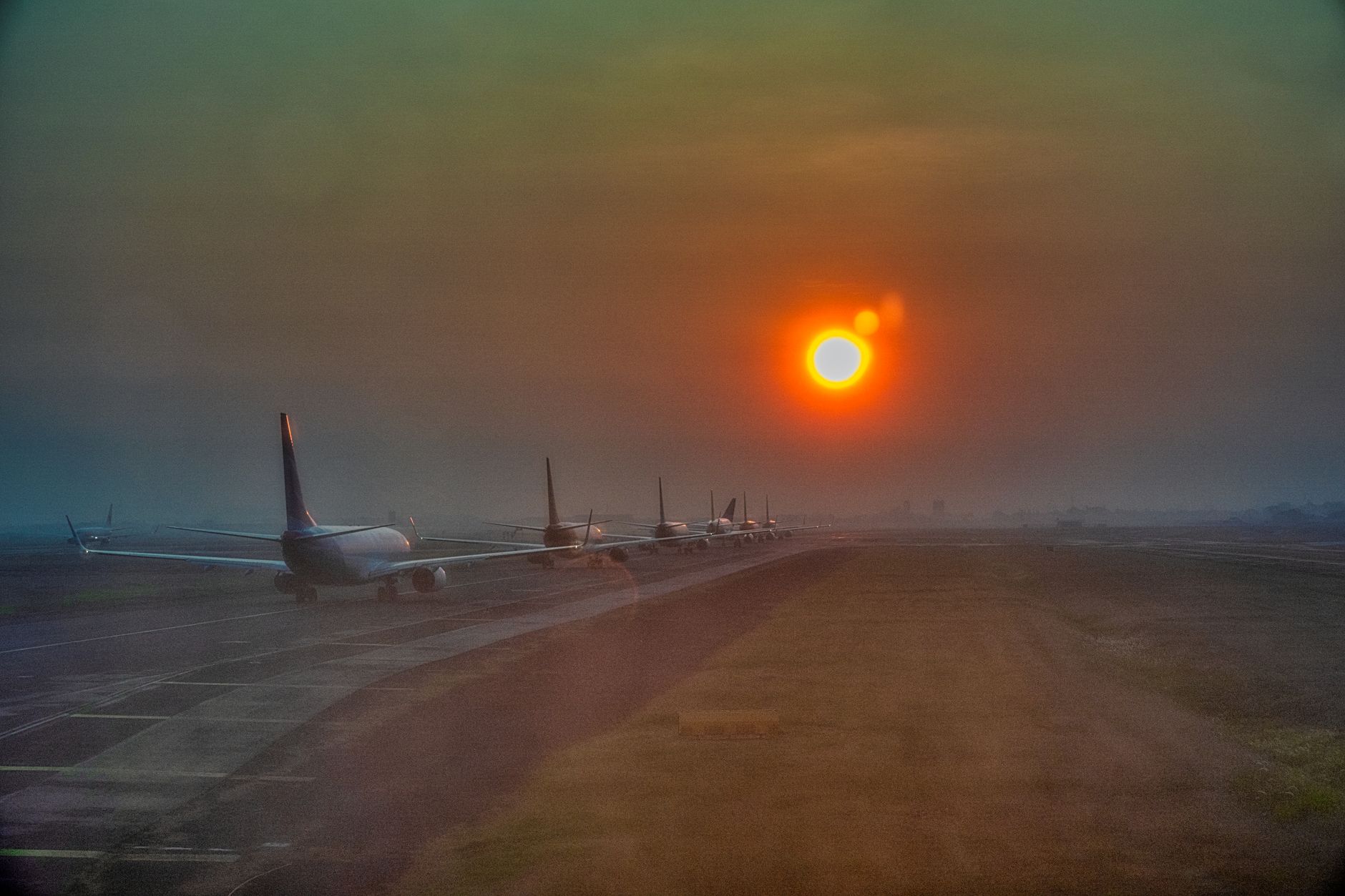A line of passenger jets queuing on a taxiway under a hazy sunset